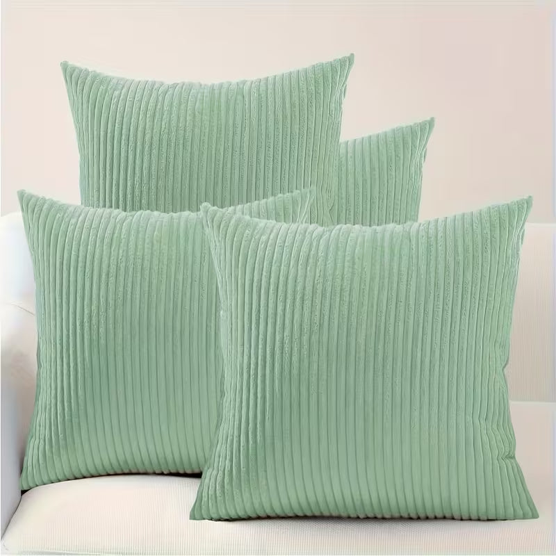 Funda de cojín verde menta de 45x45 cm con textura de pana de canalé fino sobre un sofá blanco.