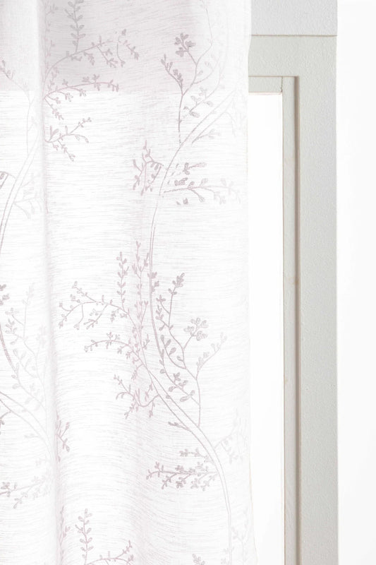 Cortina botánica blanca con estampado vegetal ligero y ojales metálicos instalada en ventana de salón luminoso.