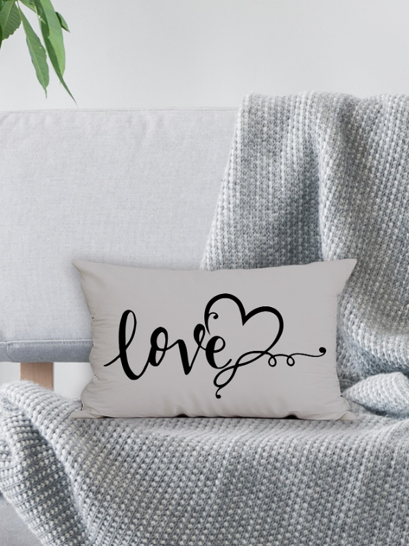 Funda de cojín gris rectangular de 30x50 cm con diseño Love y corazón sobre un sofá con manta gris.