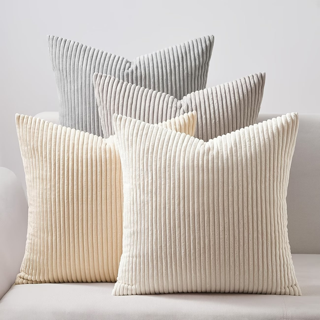Pack de 4 fundas de cojines de 40x40 cm en colores gris, beige y blanco roto sobre un sofá moderno