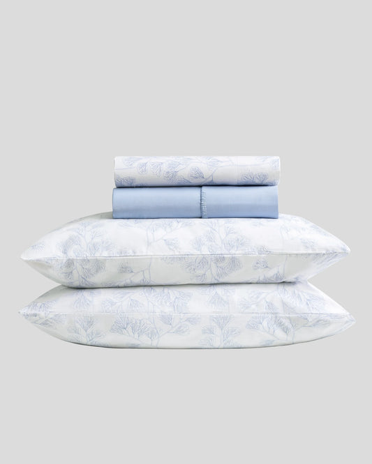 Set de sábanas de verano marca Don Algodón modelo Coralia en color azul, dobladas mostrando el estampado botánico.